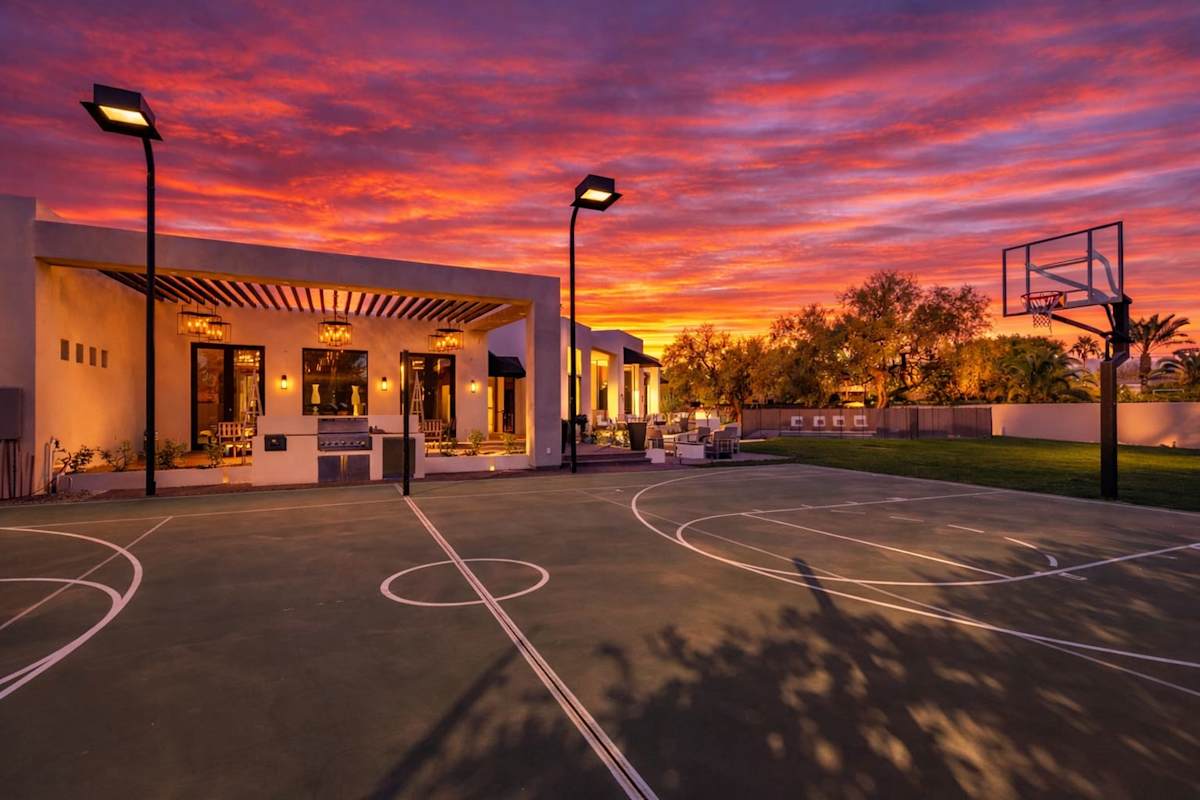 Expansive backyard paradise with a full-size basketball court, sprawling lawn, fire pit lounge, sparkling pool with oversized spa, outdoor dining for 16, and both covered and open-air patios filled wi