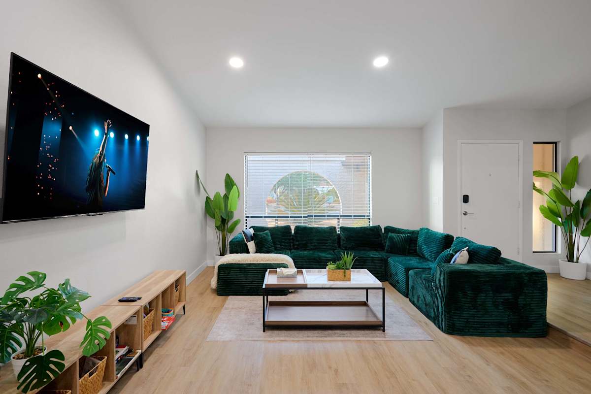 Living room comfort takes center stage with a channel-tufted emerald sectional, wall-mounted TV, and lush potted greens against warm oak floors.