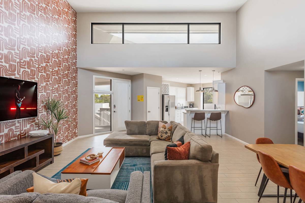 Spacious living room with soaring ceilings, a plush sectional, Smart TV, connection to dining area, and an open concept flow to the kitchen and easy access to the private balcony.