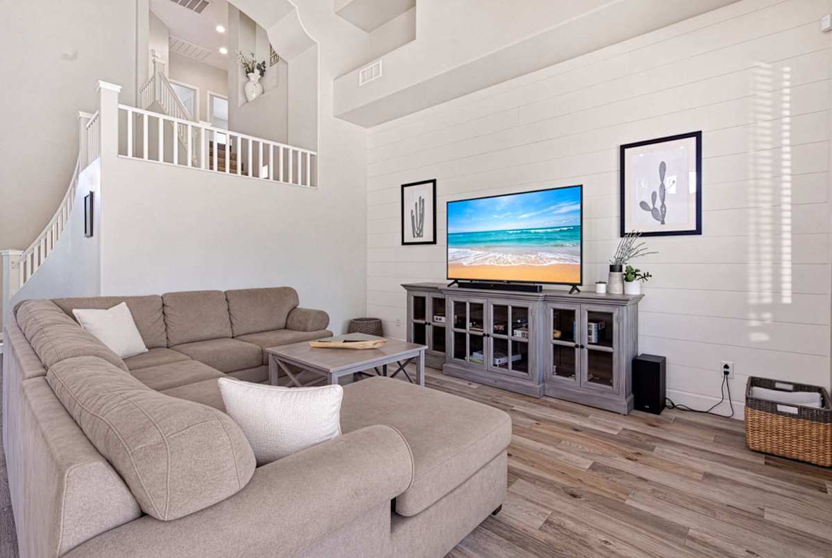This living room's vaulted ceilings and natural light fill an airy living space, where an oversized sectional and smart TV make for easy movie nights, just steps from sliding doors out to the pool.