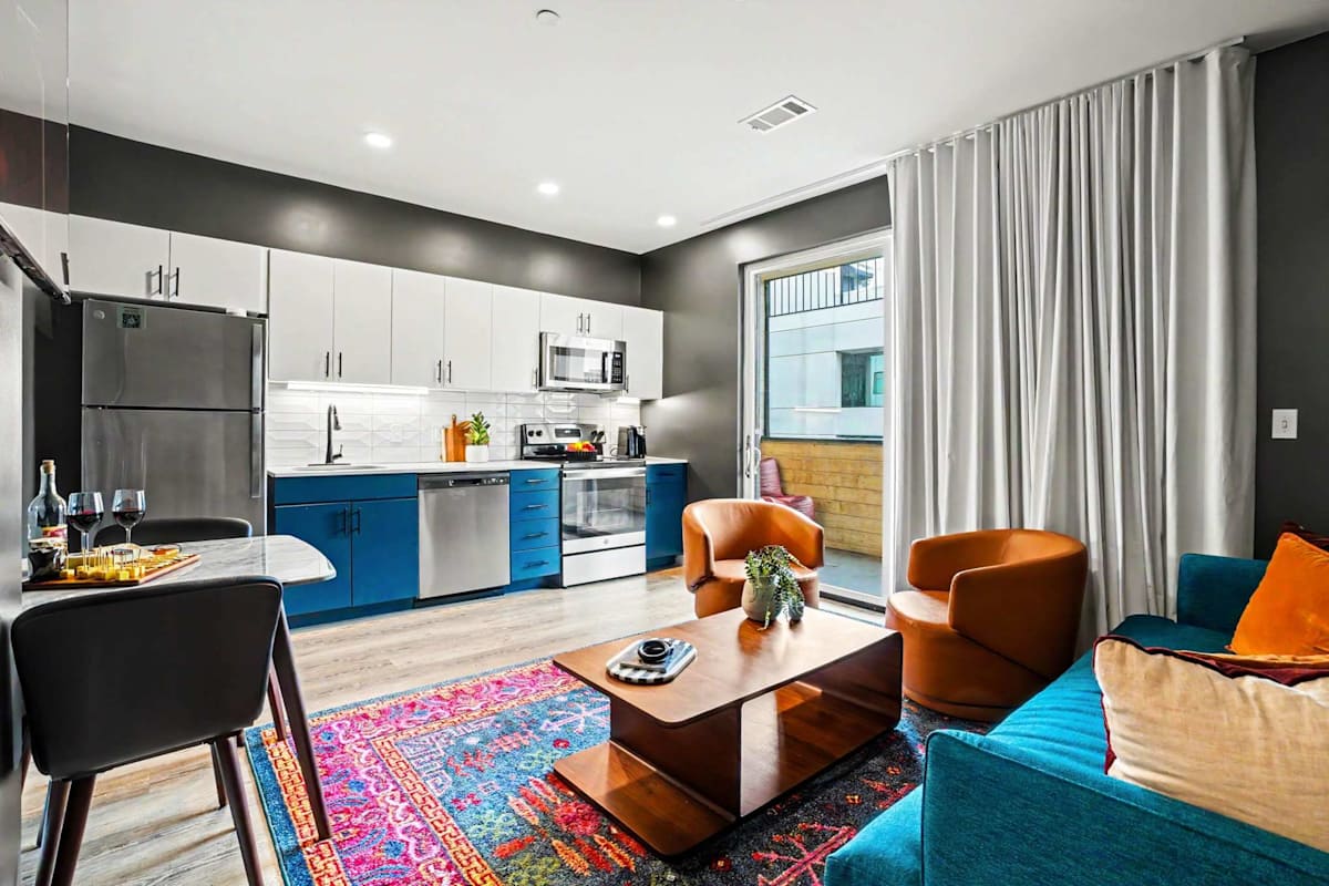 The living area brings bold personality with a teal sofa, leather swivel chairs, a sculptural wood coffee table, vibrant area rug, music-inspired art and a large smart TV.