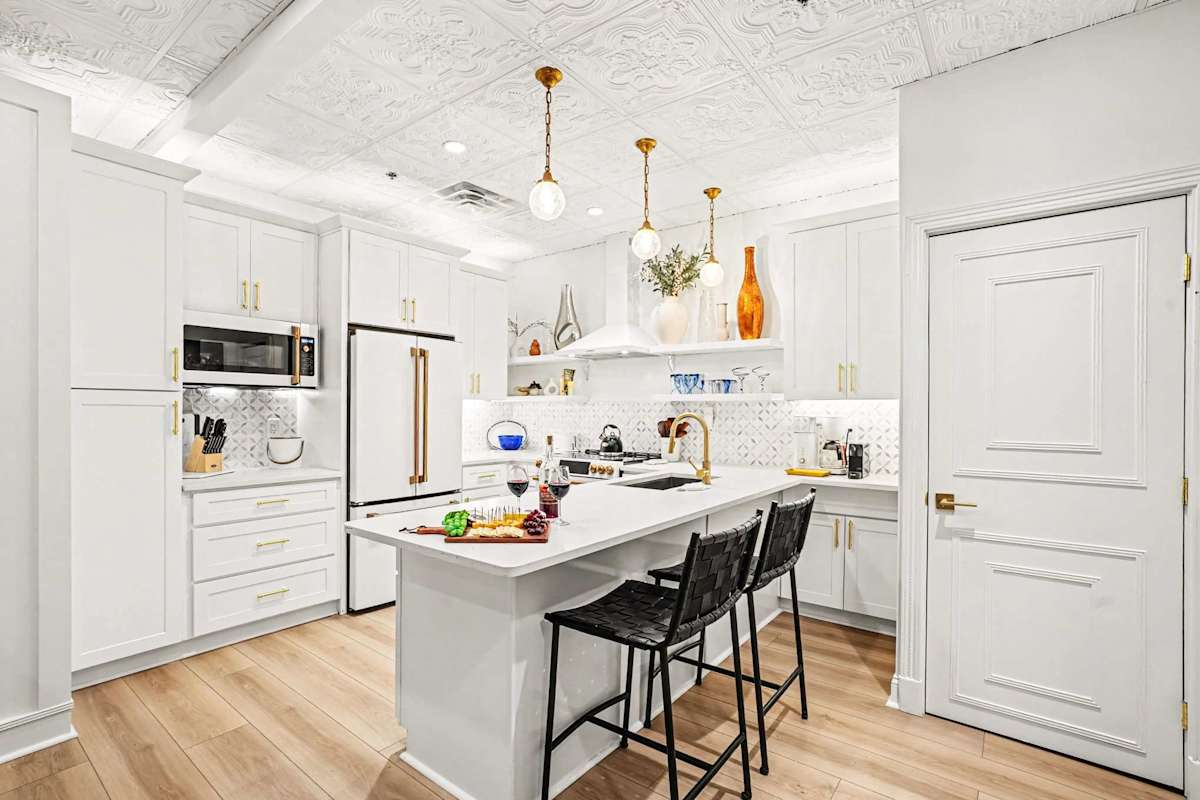This white kitchen shines with brass and gold accents, high-end appliances, and an oversized island perfect for entertaining, all under a stunning pressed-tin ceiling for character.