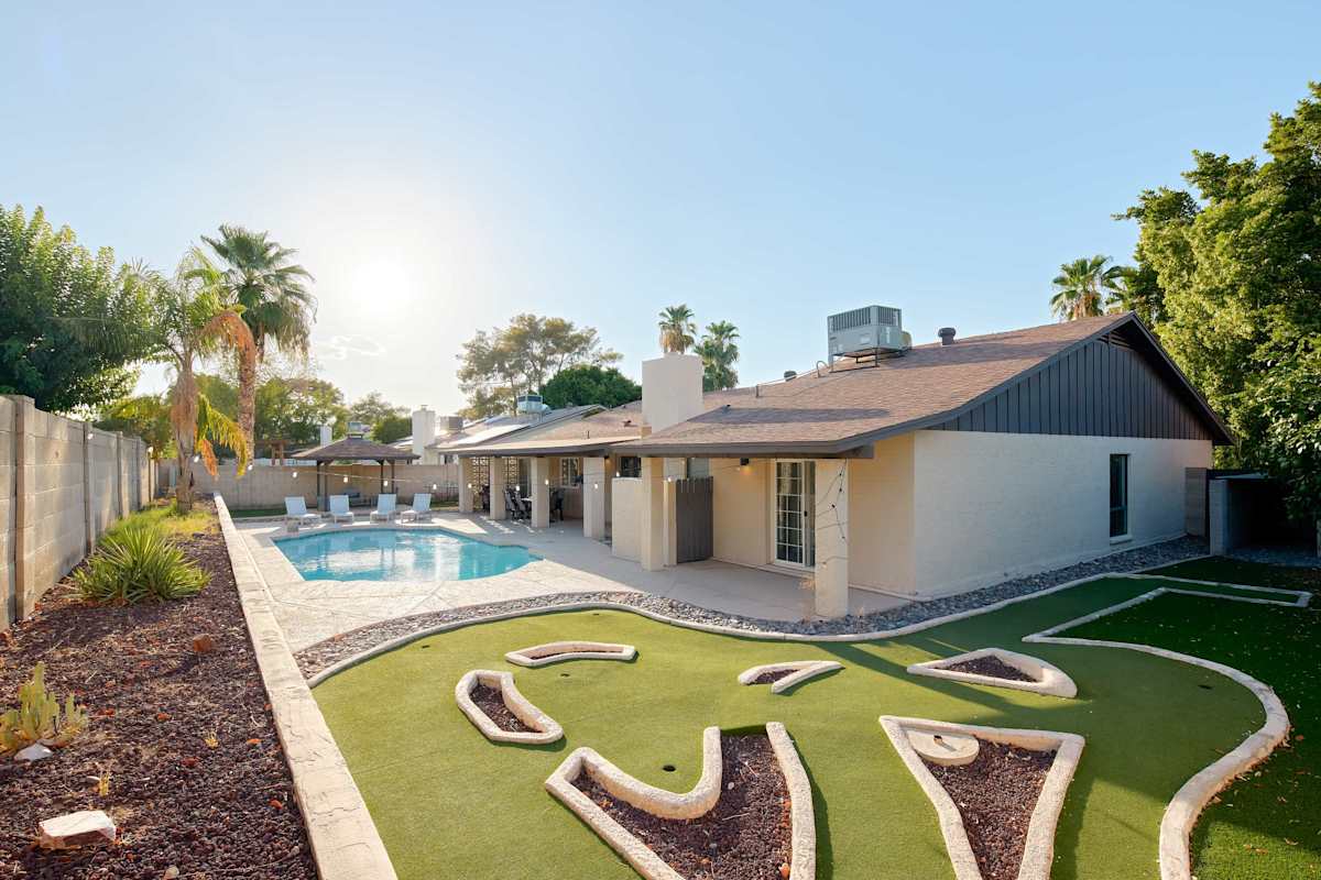 Backyard transforms into a private resort with a sparkling pool, putting green, and ping pong table. A covered patio invites dining, while a separate pergola lounge sets the stage for golden-hour cock
