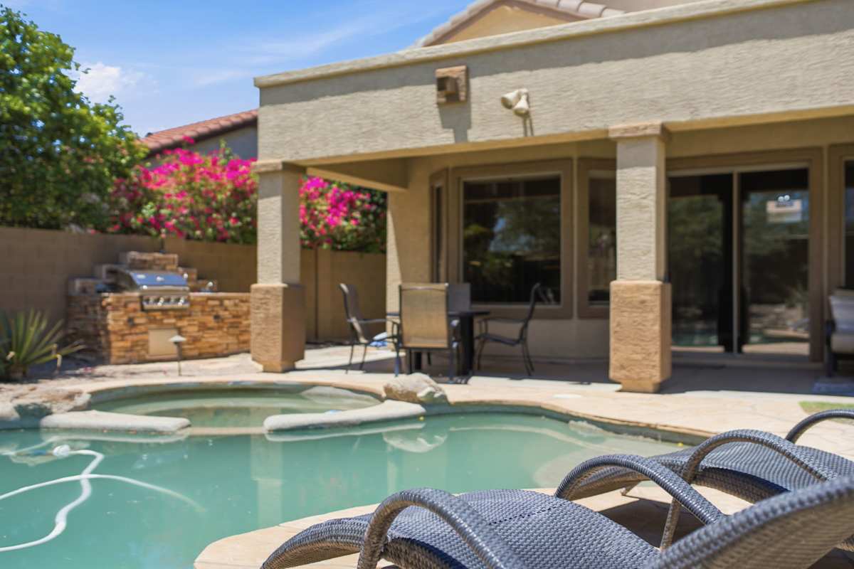 This backyard centers around a pebble-finish pool and spa, with a covered patio, fire pit lounge, dining area, and built-in stone BBQ for easy outdoor entertaining.