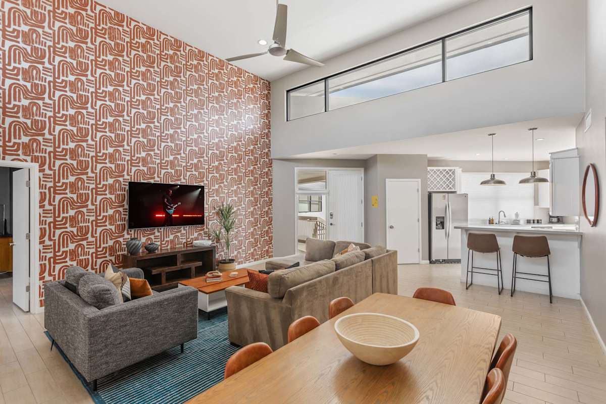 Spacious living room with soaring ceilings, a plush sectional, Smart TV, connection to dining area, and an open concept flow to the kitchen and easy access to the private balcony.