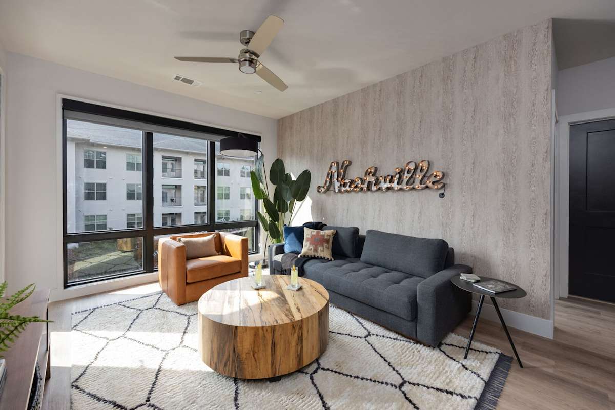 Modern open concept living area with floor to ceiling windows, designer furniture, smart TV, and access to private patio.