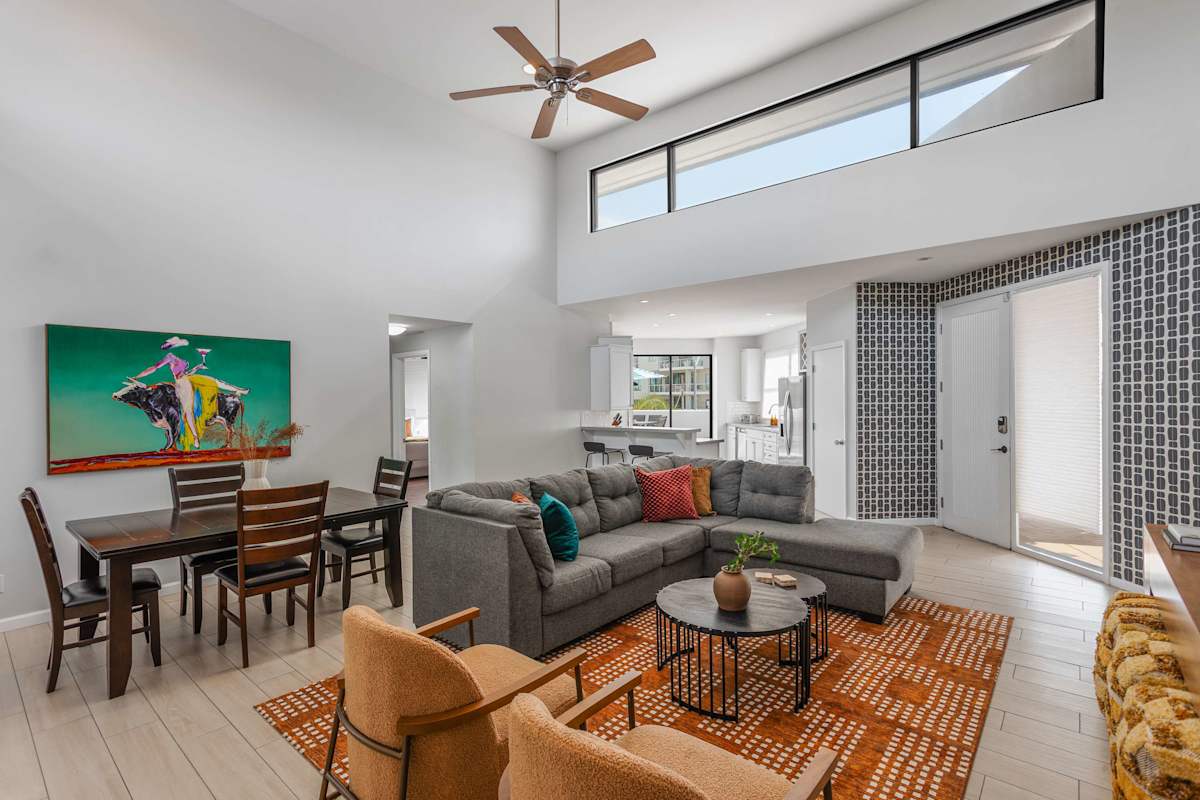 Bright and open living room with soaring ceilings, oversized windows, a plush sectional, Smart TV, and easy flow to the dining area for 4, kitchen, and balcony.