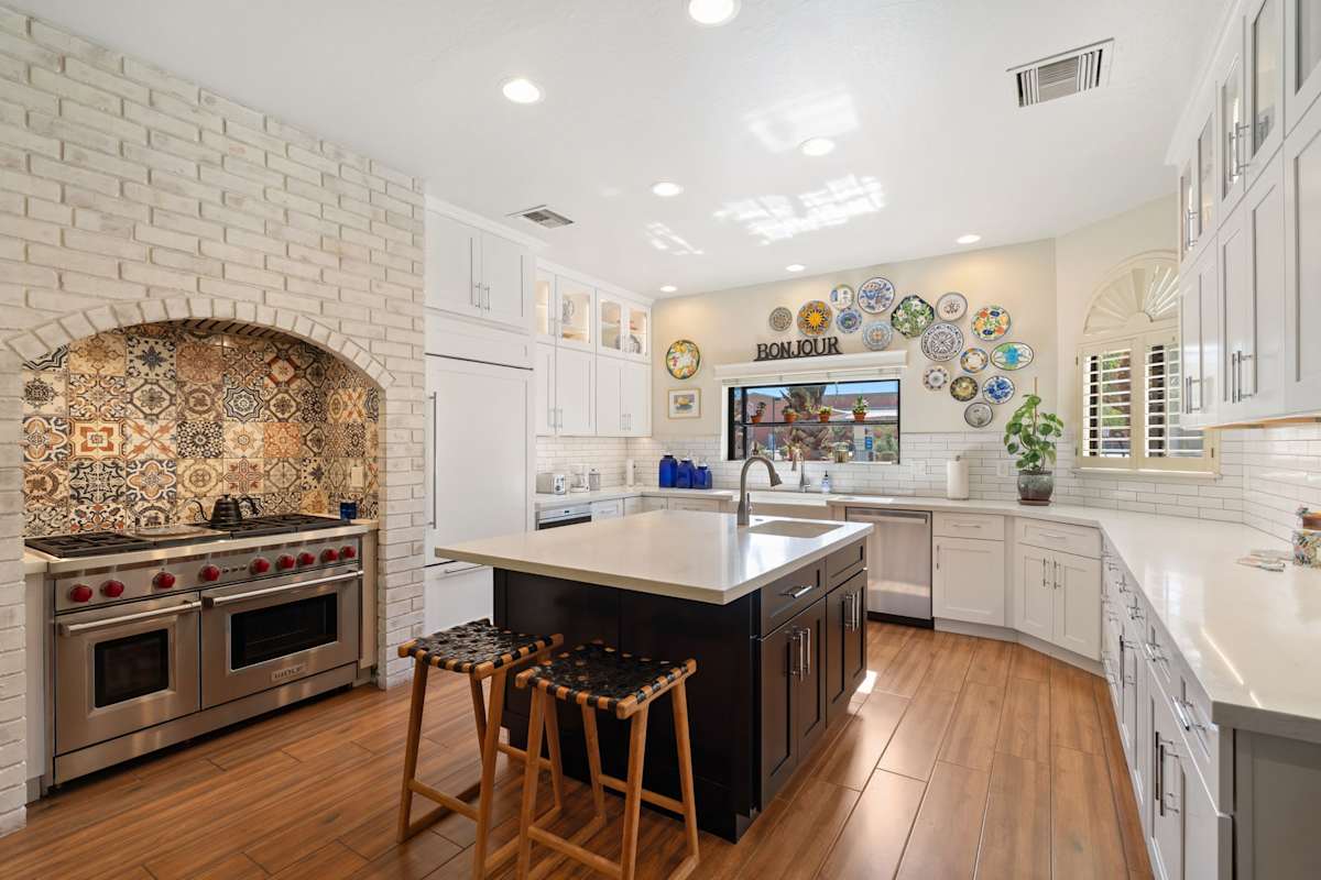 Bright chef’s kitchen with a Wolf range, bold tile backsplash, spacious island with seating, and generous counter space for effortless meals.
