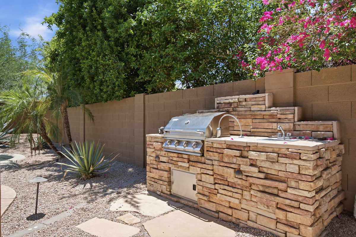 This backyard centers around a pebble-finish pool and spa, with a covered patio, fire pit lounge, dining area, and built-in stone BBQ for easy outdoor entertaining.