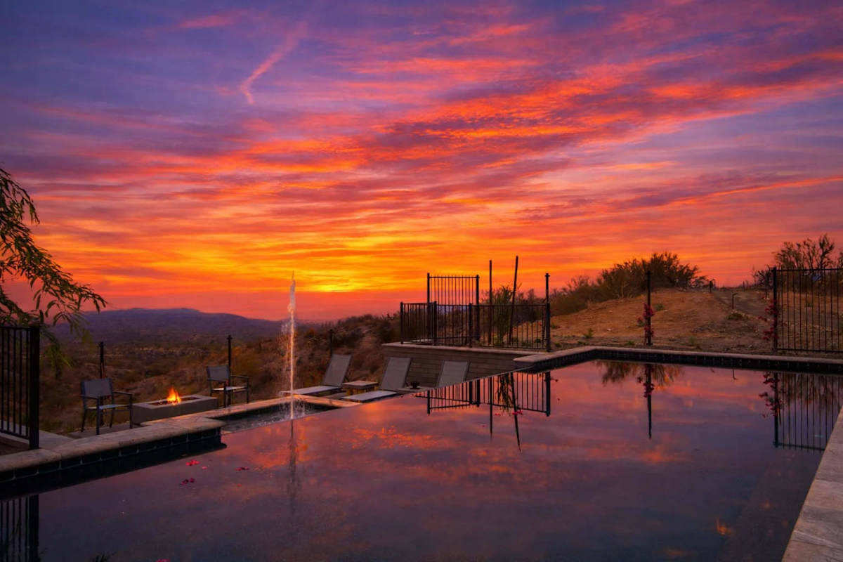 Stunning private oasis featuring a sparkling heated infinity pool and spa with sun loungers, a patio with a BBQ grill, multiple lounge areas, and fire pits surrounded by unparalleled desert views.