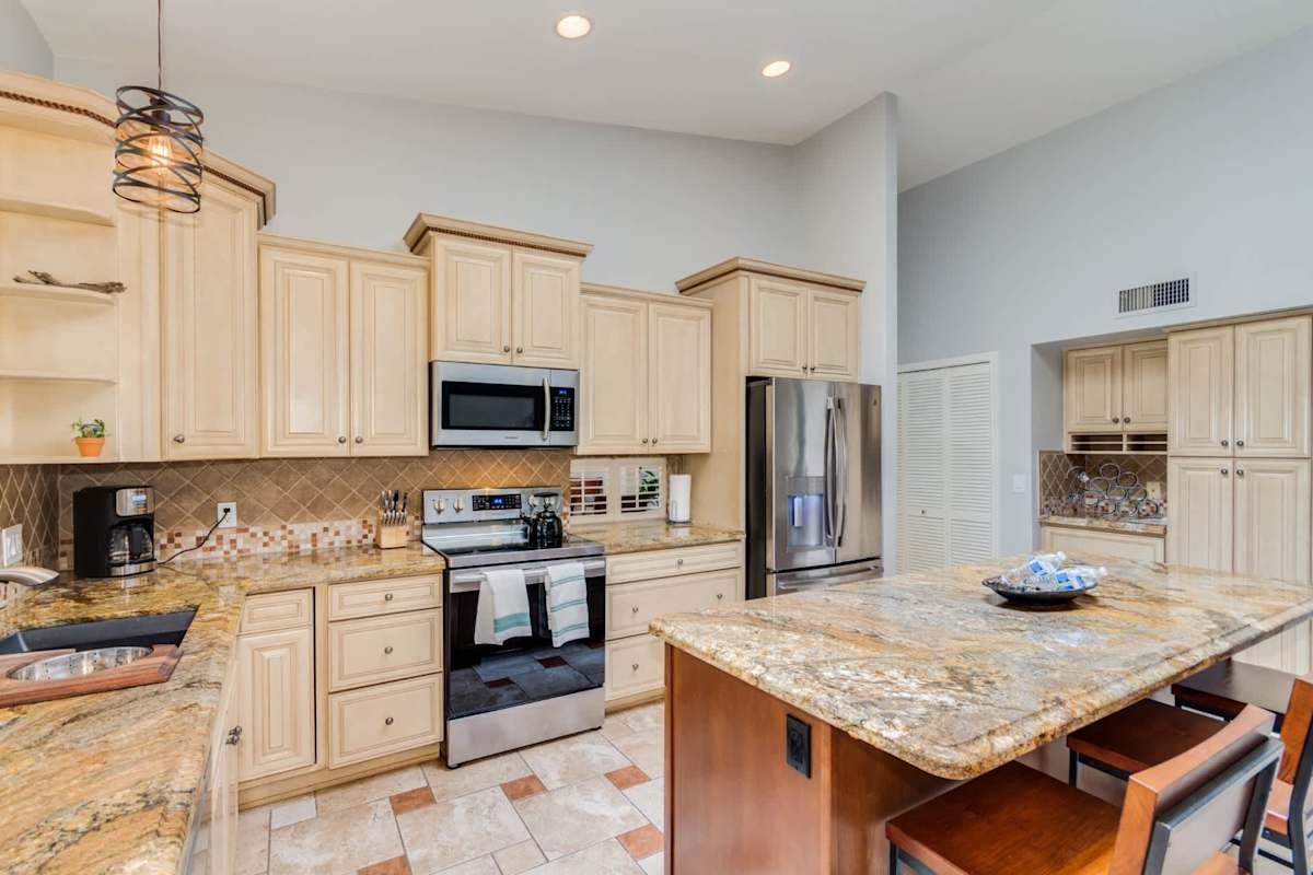 Open concept kitchen with stainless steel appliances, granite countertops, kitchen island with breakfast bar seating for 3, and coffee maker