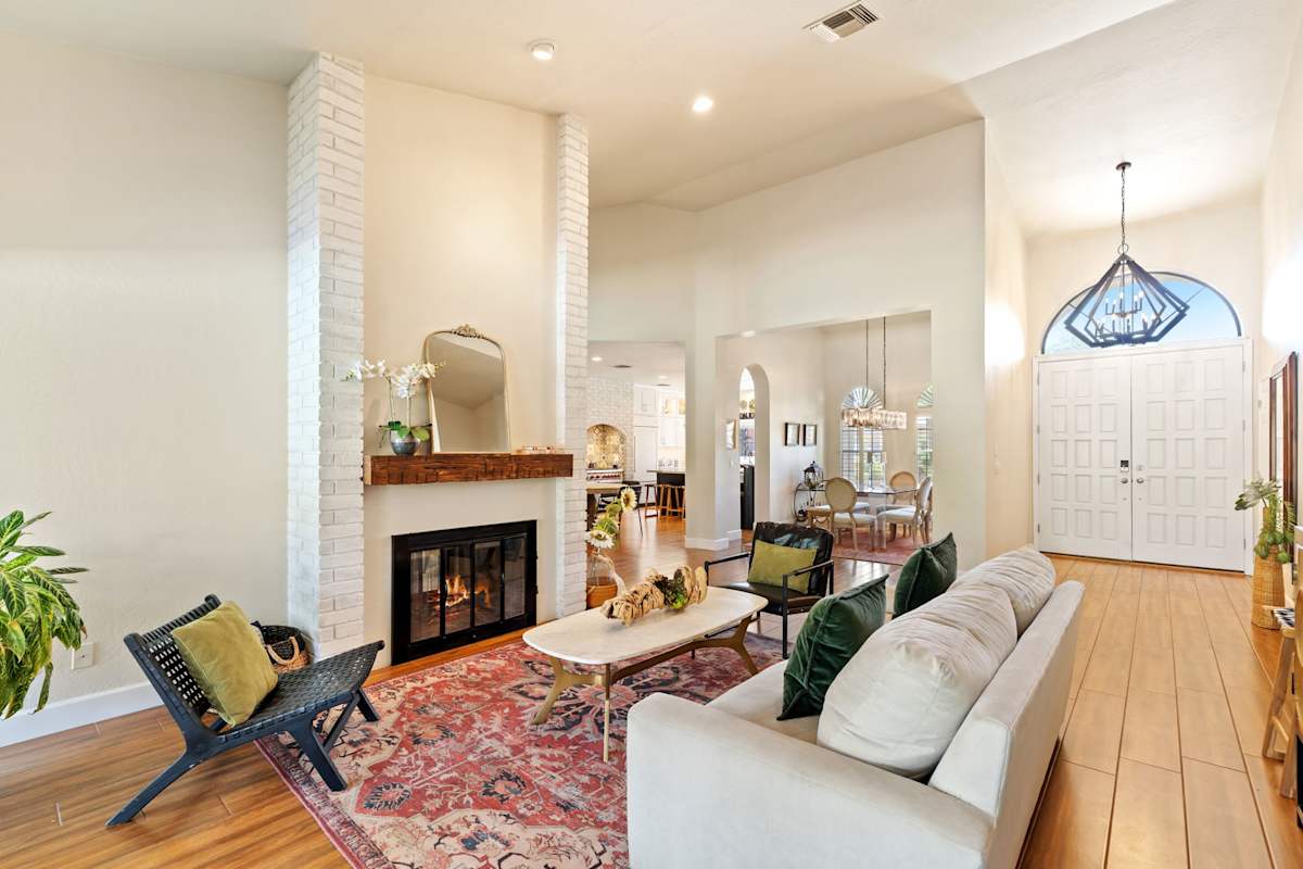 Unwind in this dual living room featuring two stylish lounging areas anchored by a double-sided white-brick fireplace, complete with a Smart TV, vaulted ceilings, and sunlit views toward the poolside 