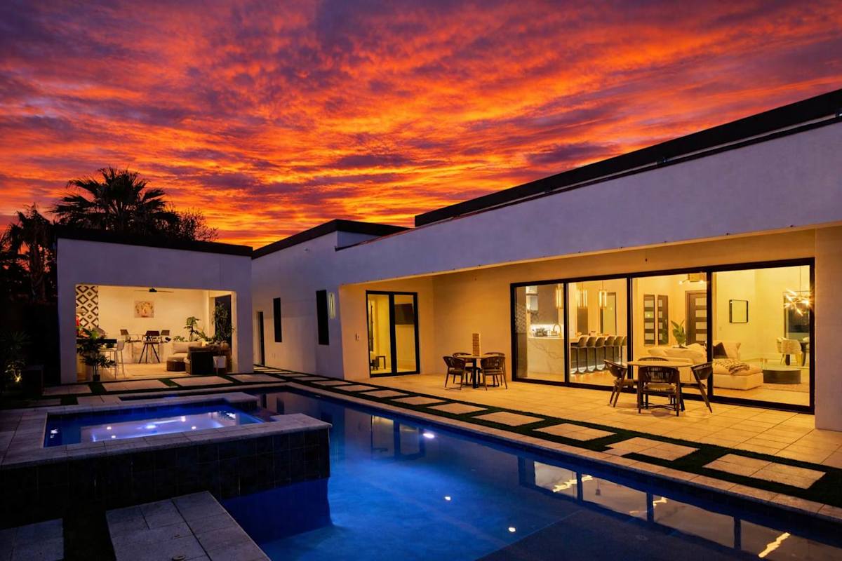 Resort-style backyard featuring a covered patio with outdoor dining, a sparkling blue heated pool and spa with sun loungers and cabanas, an outdoor kitchen with a built-in BBQ, mini fridge, and sink,