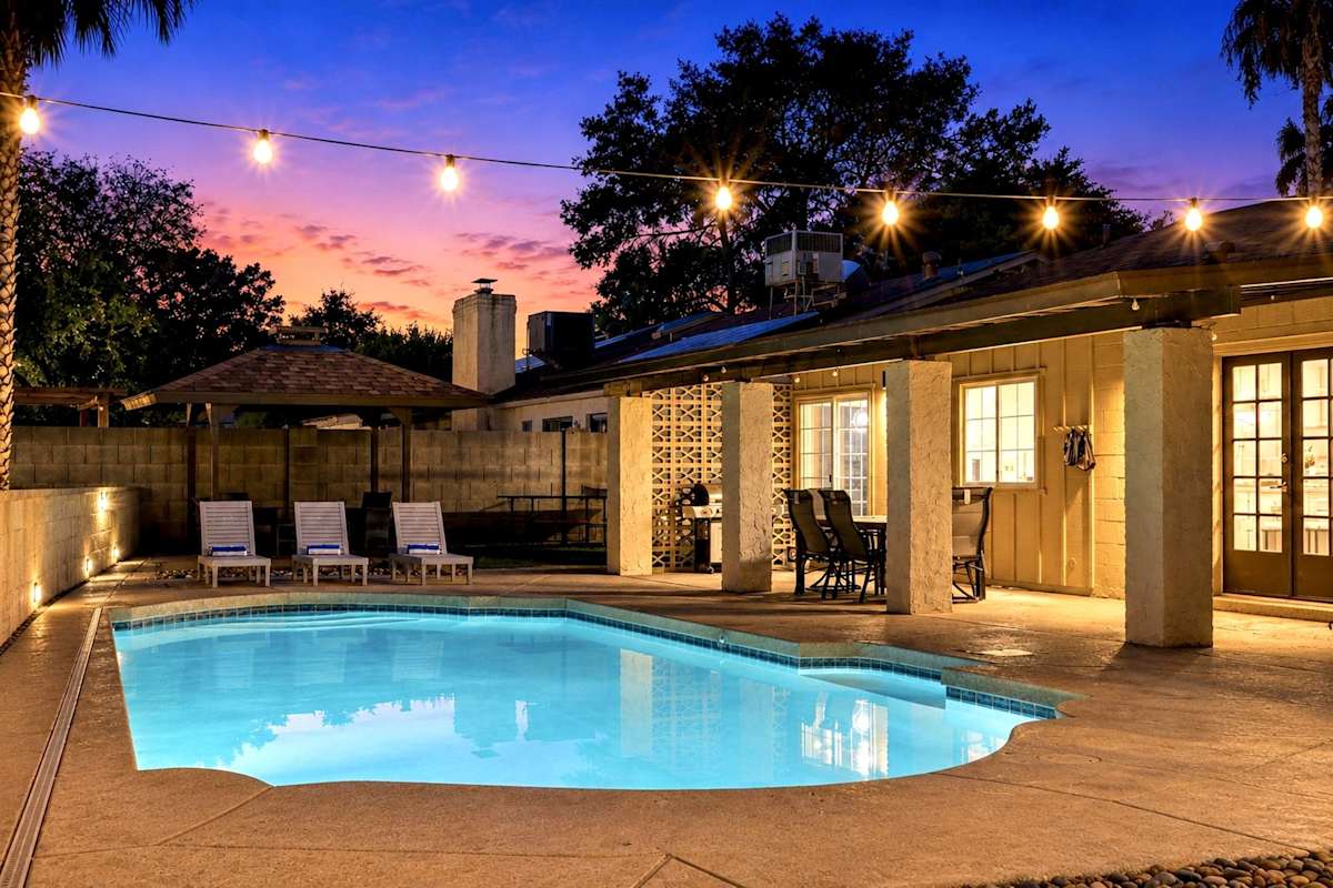 Backyard transforms into a private resort with a sparkling pool, putting green, and ping pong table. A covered patio invites dining, while a separate pergola lounge sets the stage for golden-hour cock